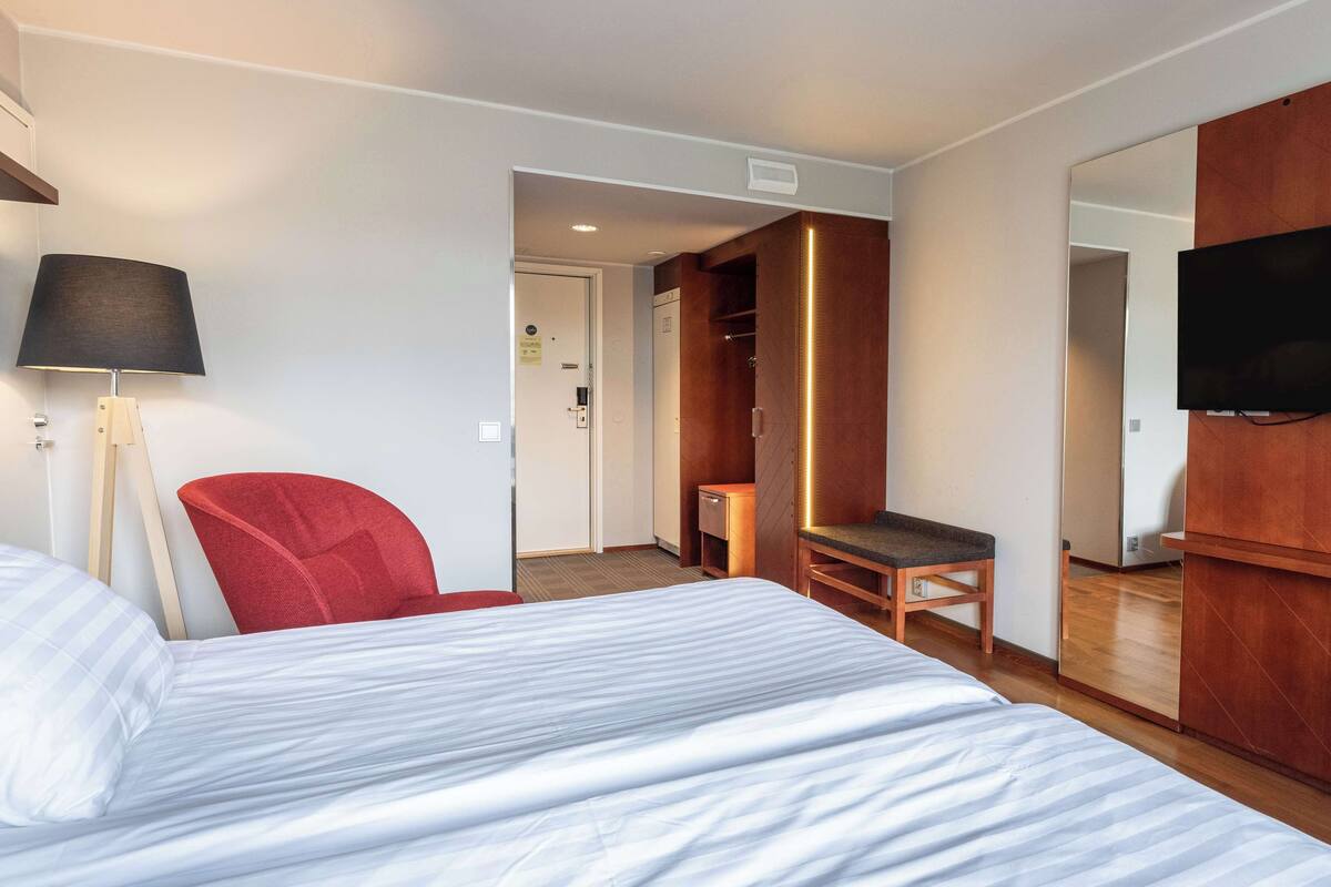 Ein Hotelzimmer mit einem Bett, einem roten Sessel, einem Schreibtisch, einem Fernseher und einem Kleiderschrank.