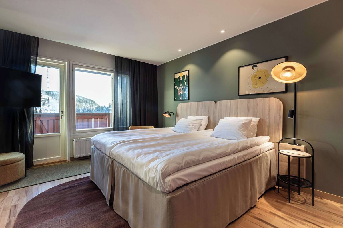 Ein modernes Schlafzimmer mit einem großen Bett, einem Nachttisch, einem Sessel und Blick ins Freie.