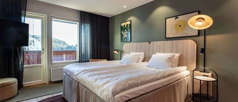 A modern bedroom with a large bed, a bedside table, a chair, and a view of the outdoors.