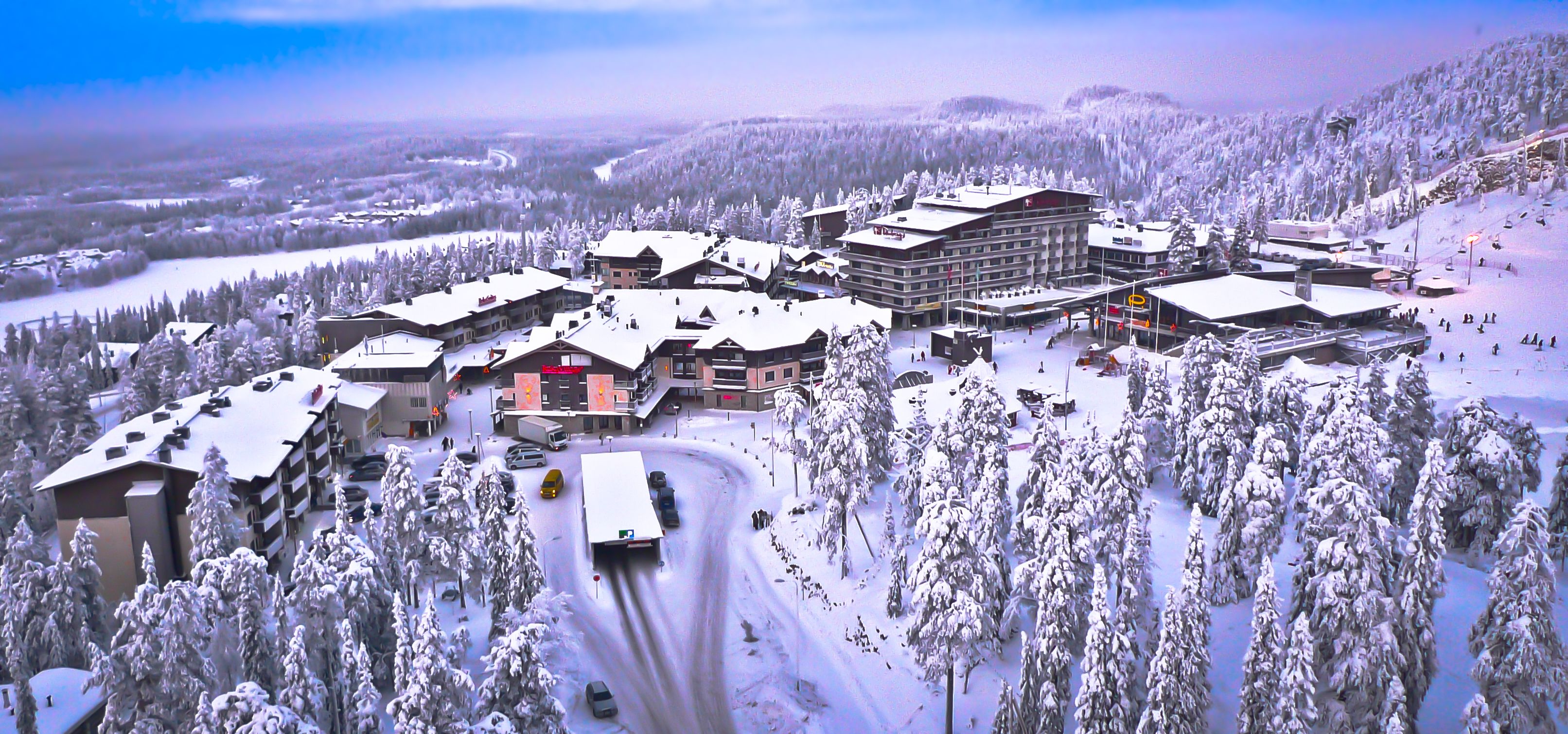 Un complejo turístico cubierto de nieve con varias edificaciones, un telesilla y una carretera serpenteante.