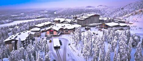 Un complejo turístico cubierto de nieve con varias edificaciones, un telesilla y una carretera serpenteante.