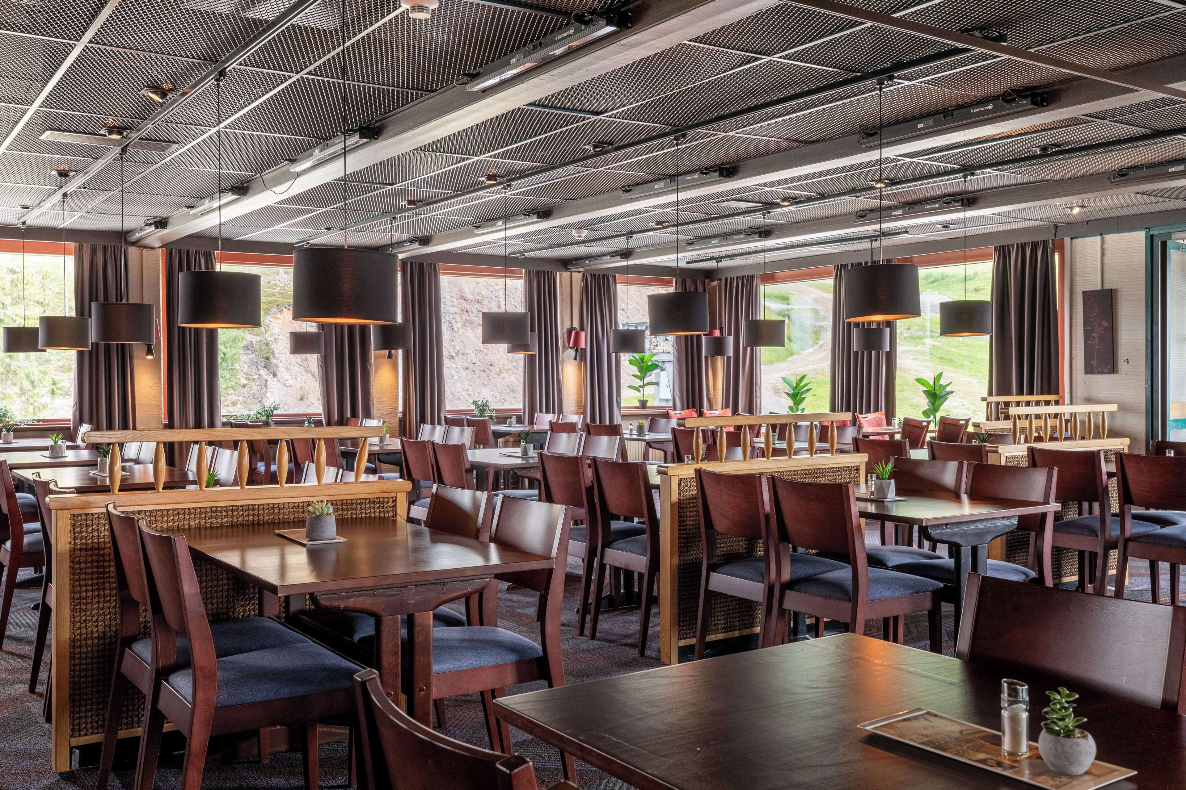 A spacious restaurant with high ceilings, modern pendant lighting, and large windows offering views of the outdoors.