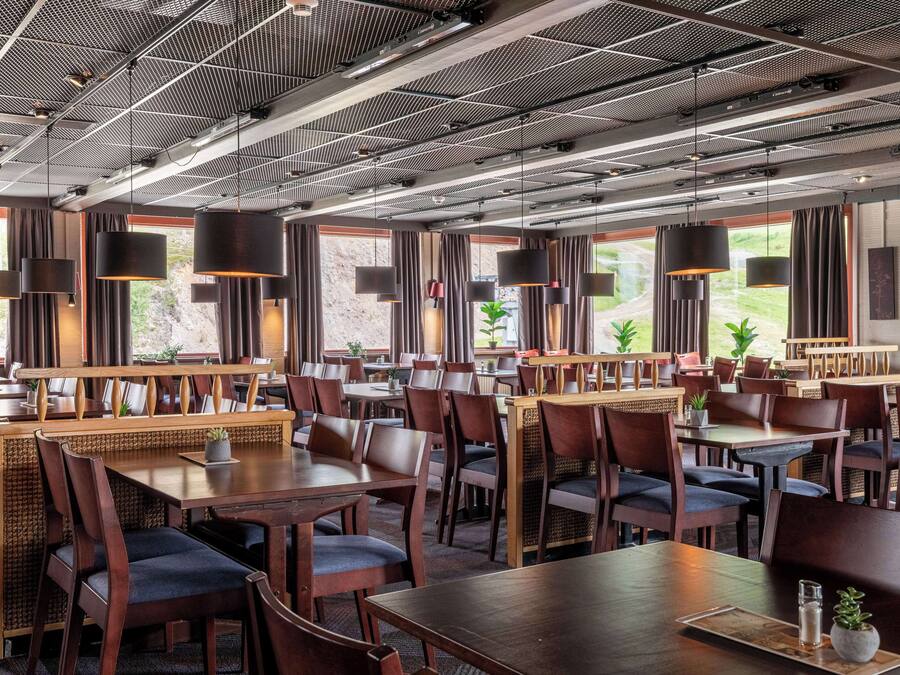 A spacious restaurant with high ceilings, modern pendant lighting, and large windows offering views of the outdoors.