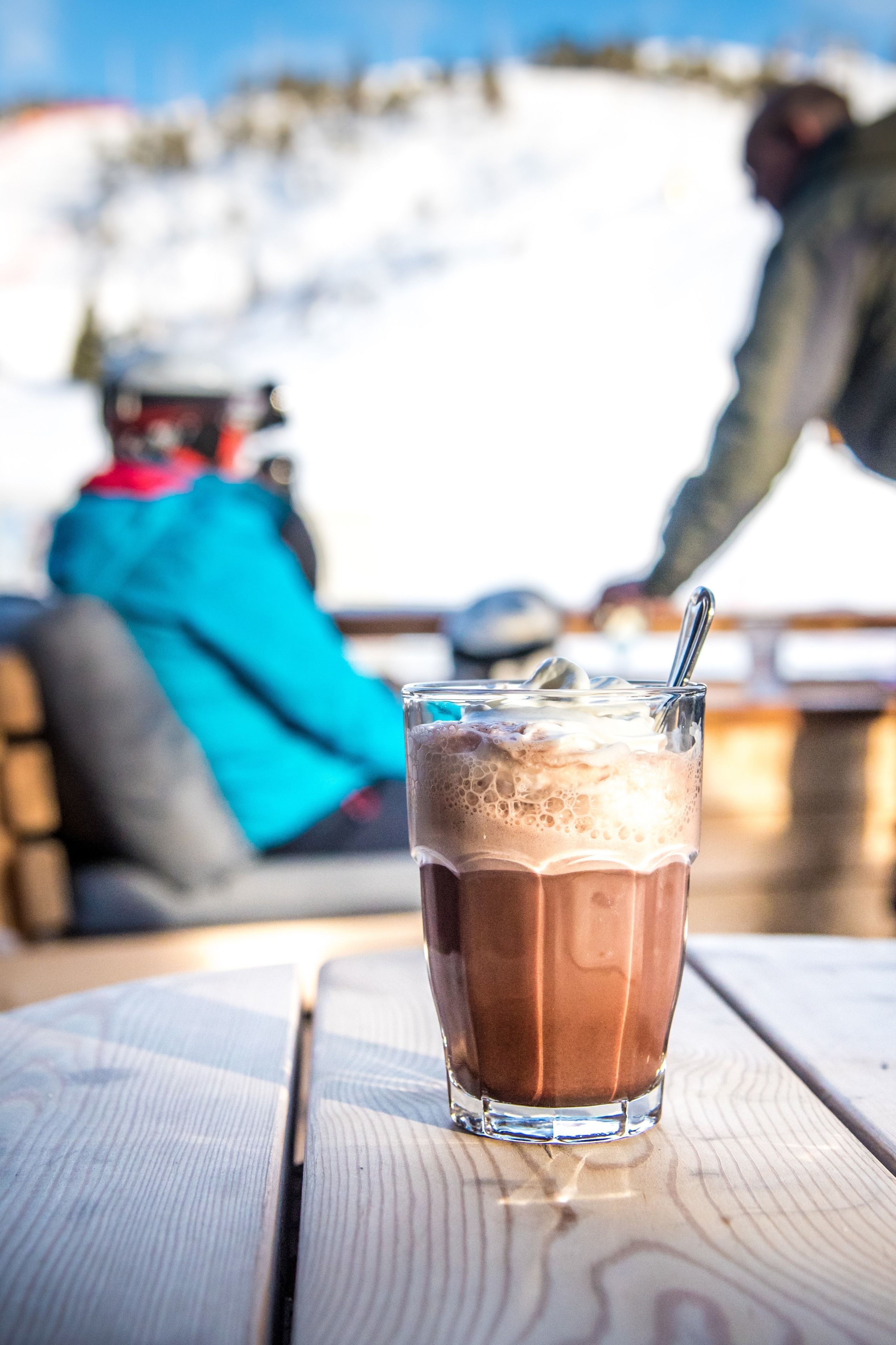 Un verre de chocolat chaud sur une table en bois, avec un paysage enneigé en arrière-plan.