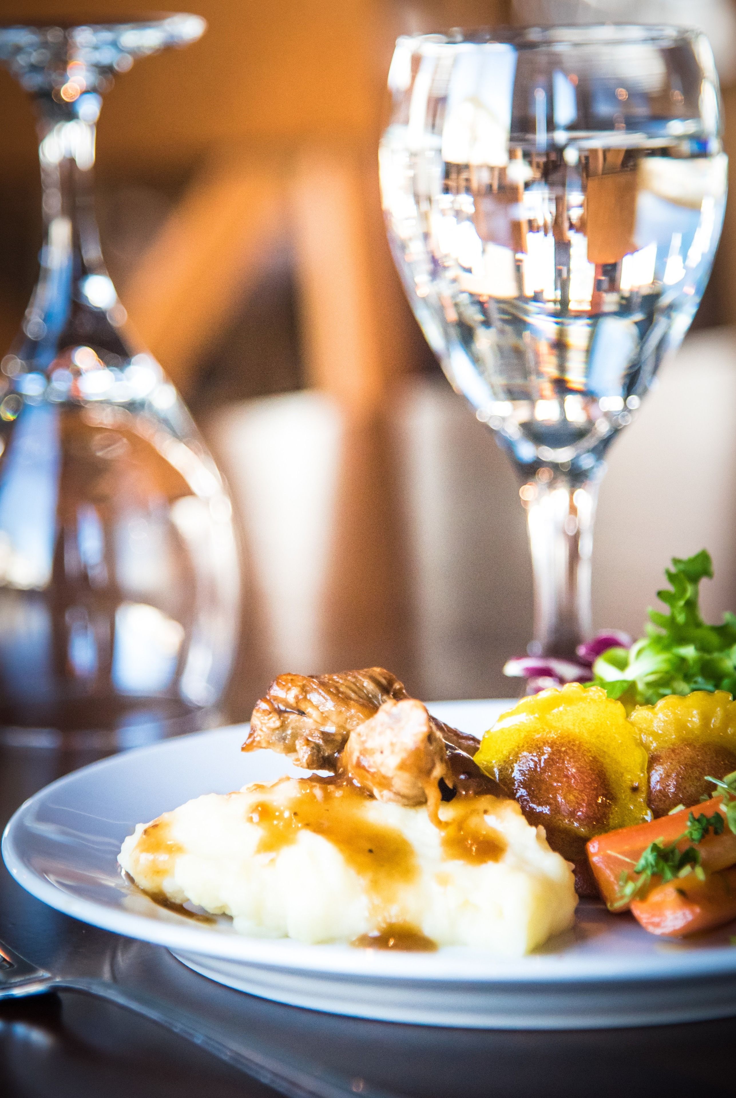 A plate of food with mashed potatoes, meat, and vegetables, accompanied by a glass of water.