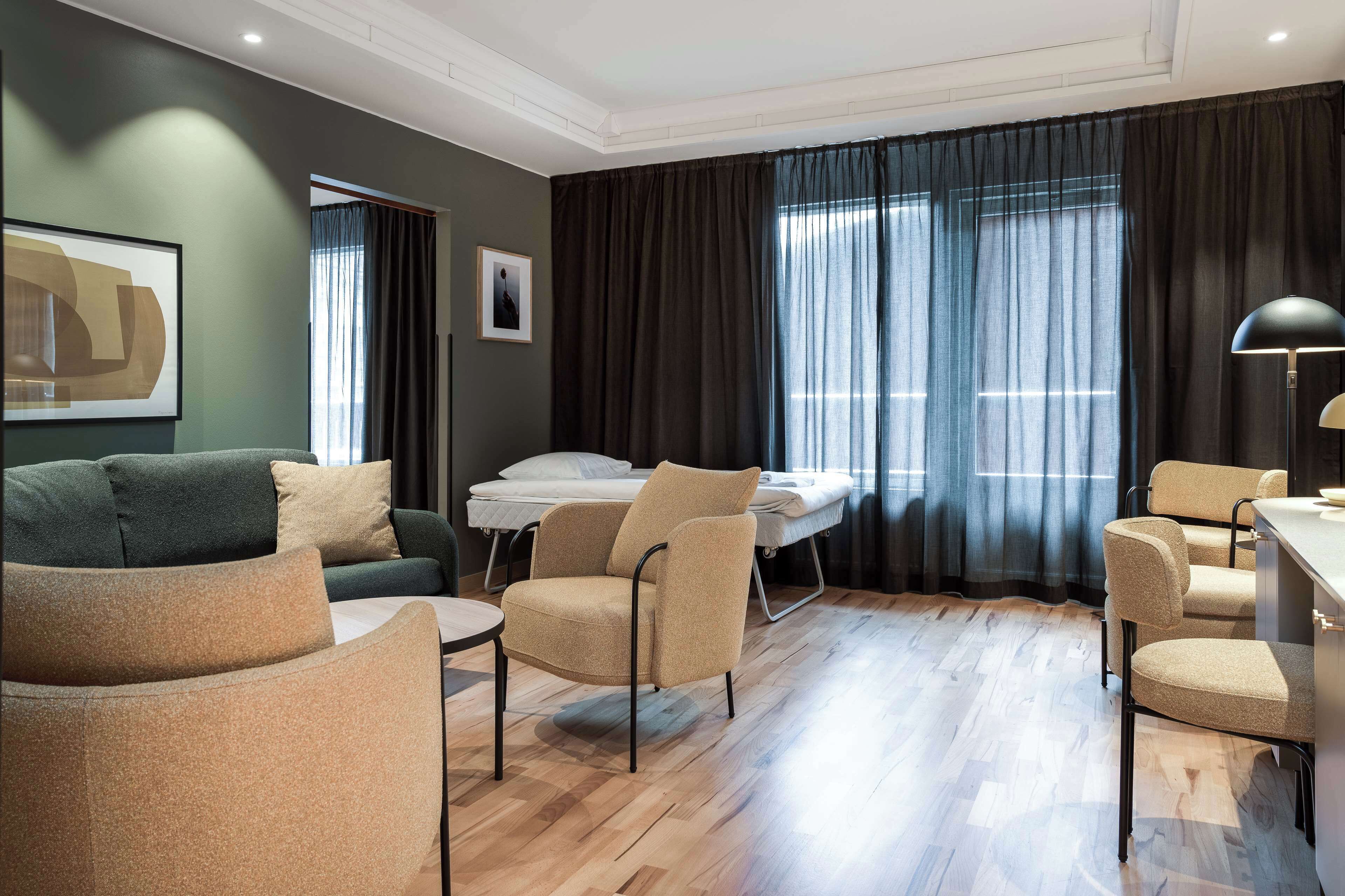 A modern hotel room with a sofa, armchairs, a bed, and a desk.