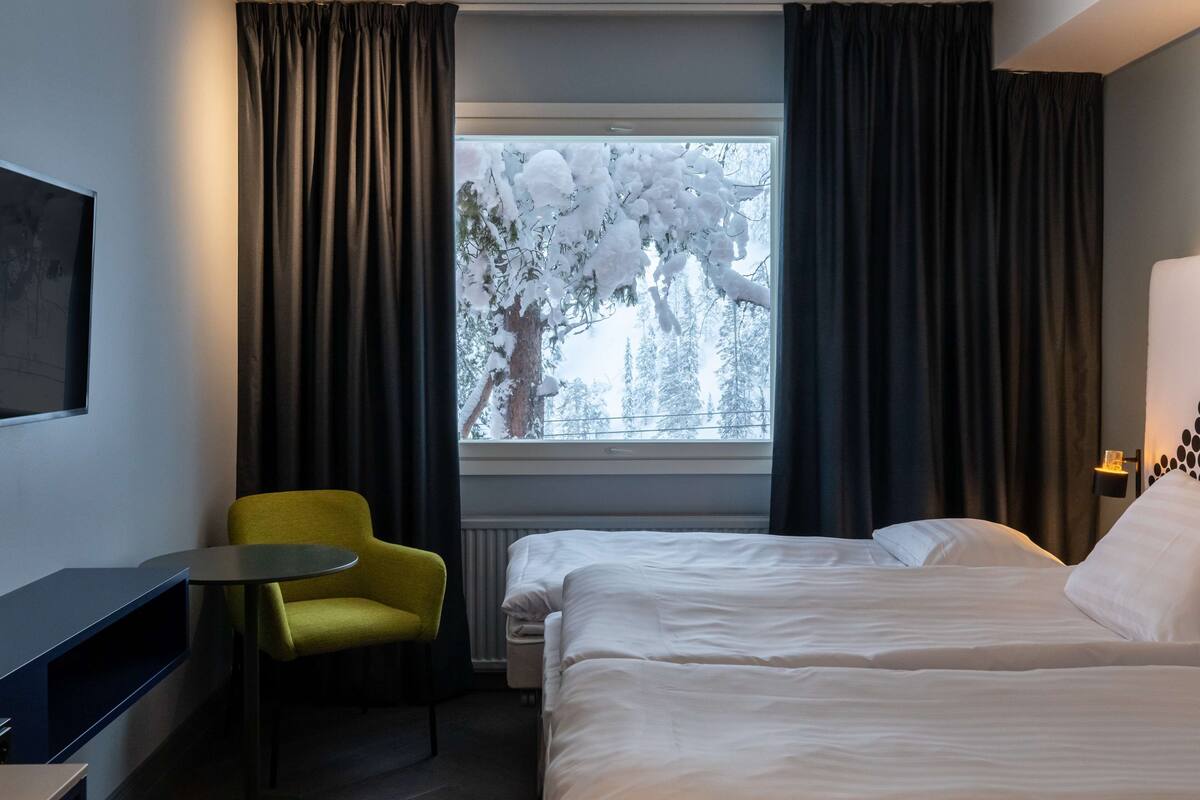 Ein Hotelzimmer mit einem Bett, einem kleinen Tisch, einem gelben Stuhl und einem Fenster mit Vorhängen.