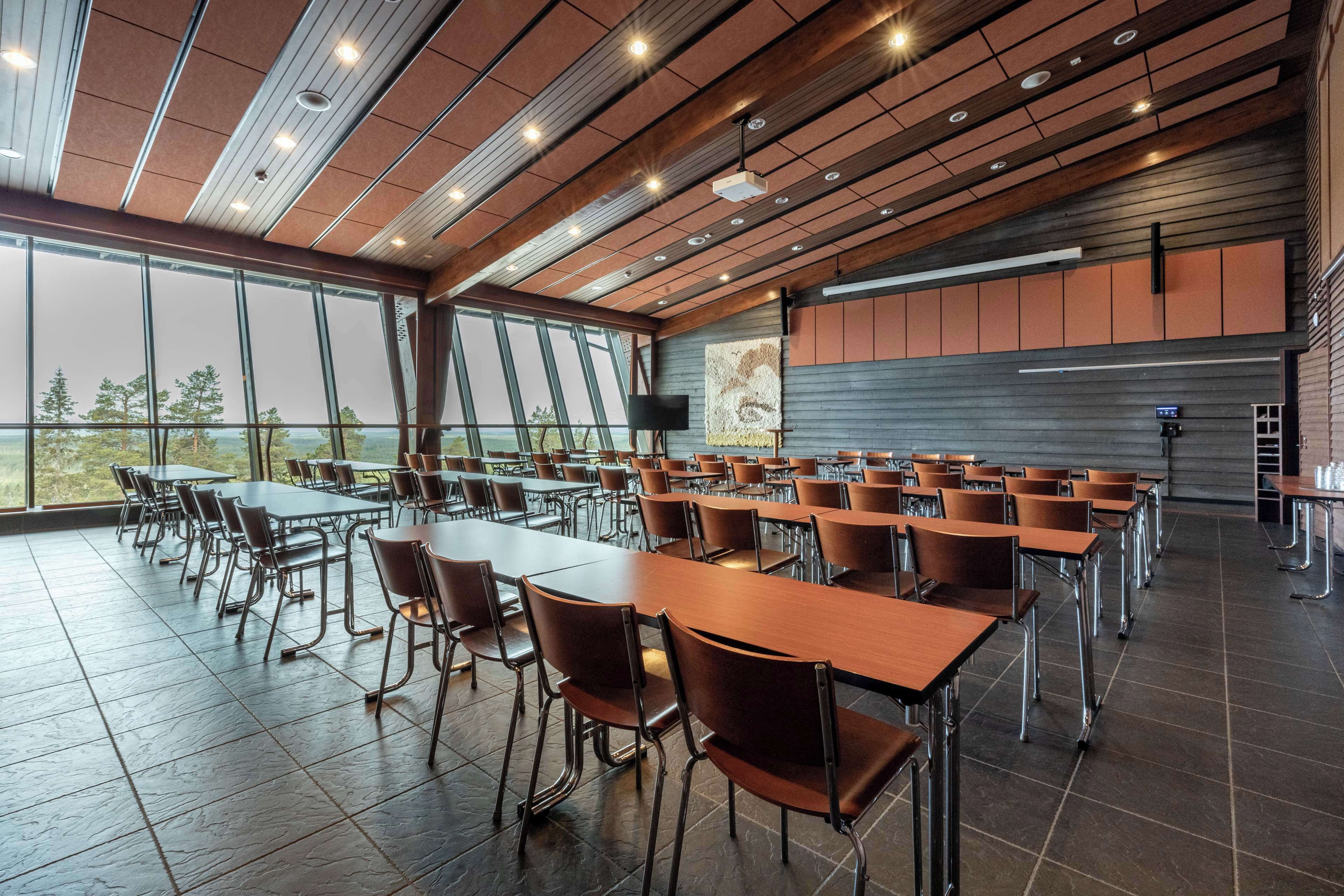 Une salle de conférence spacieuse, dotée de longues tables et de chaises, de grandes fenêtres et d’un design moderne au niveau du plafond.
