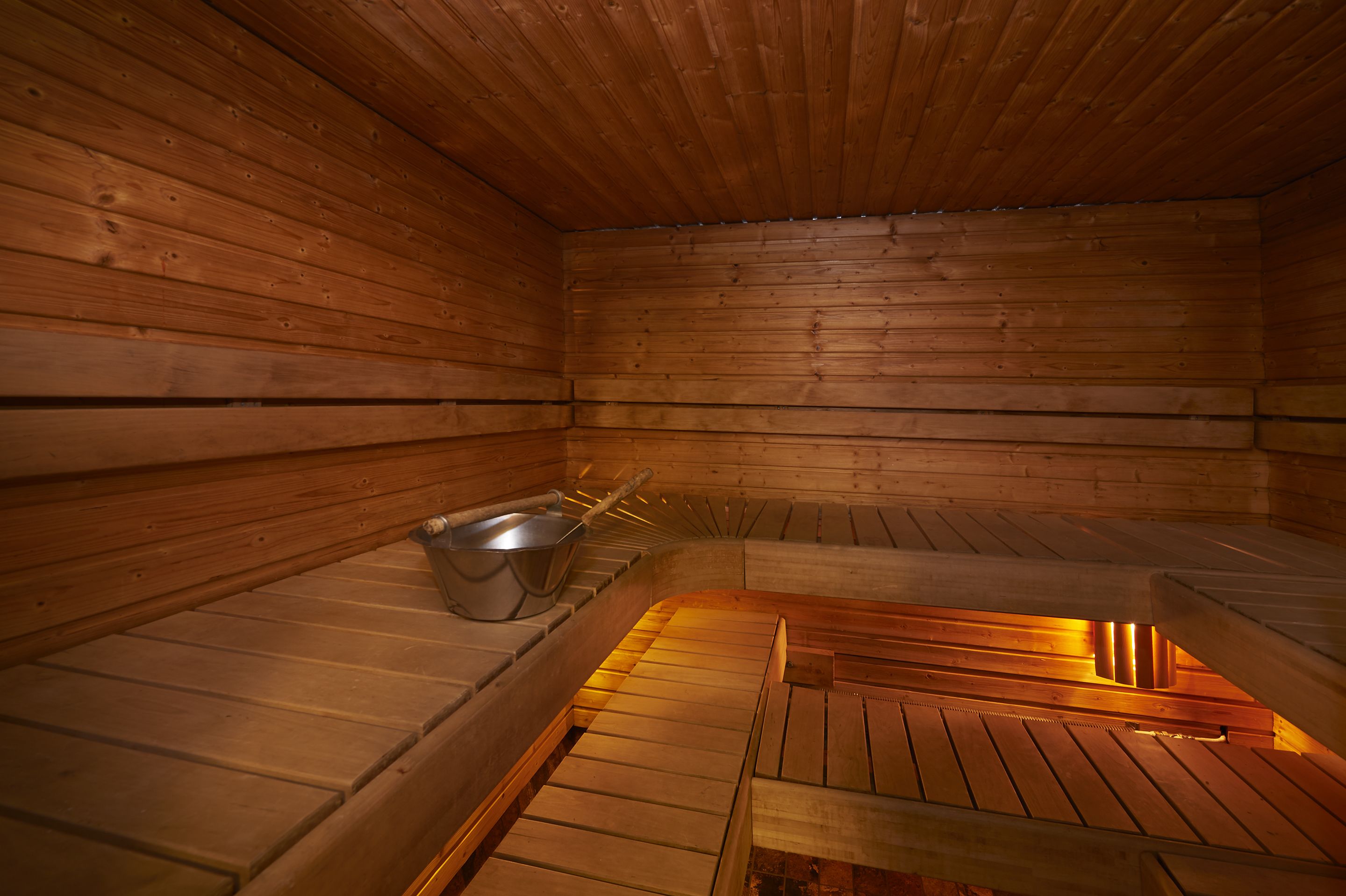 Een sauna met houten wanden en banken, een metalen wasbak en een houten vloer.