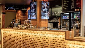 A bar area with a wooden textured counter, a coffee machine, and a display of bottled beverages.