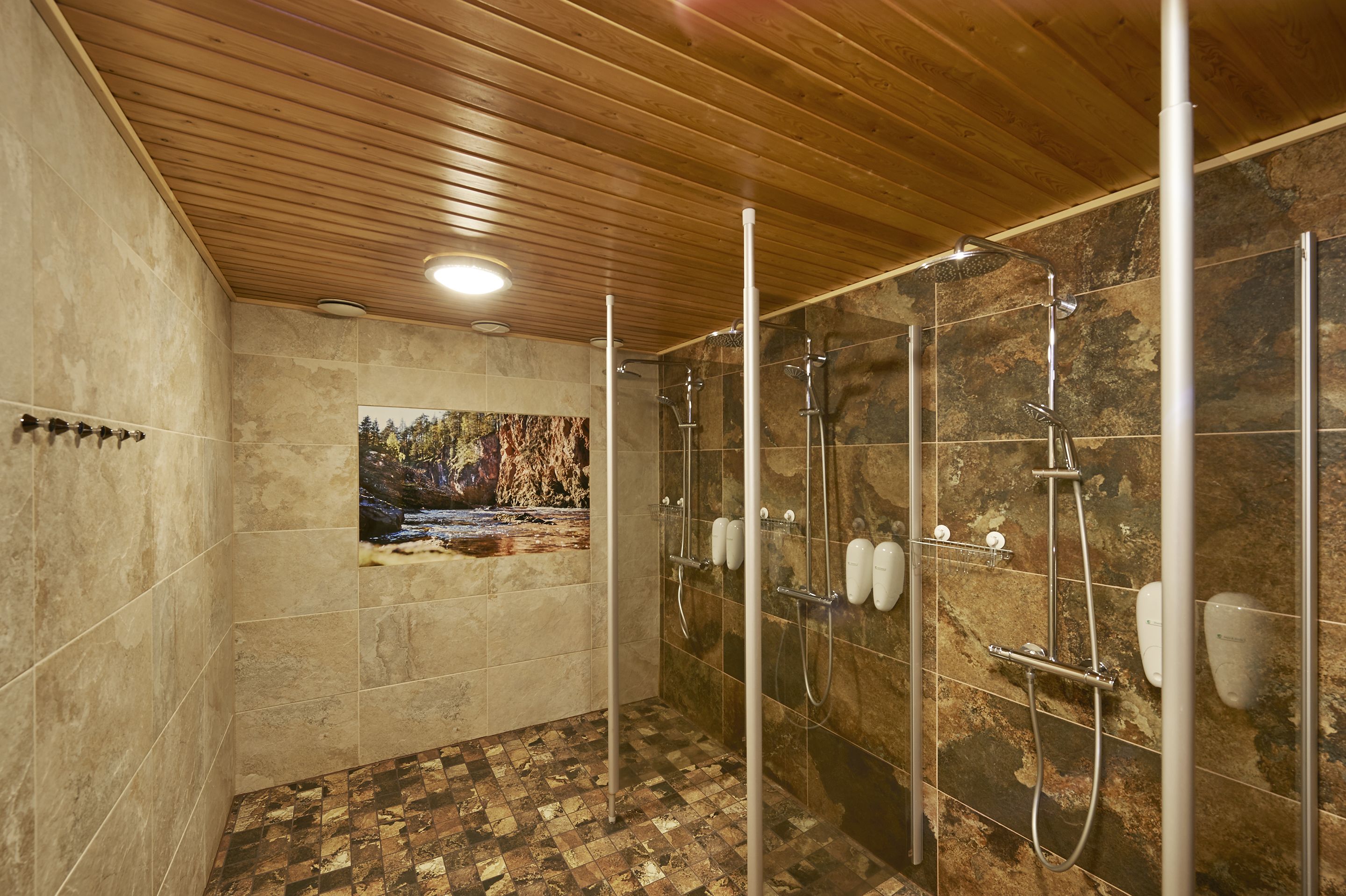 A modern shower area with multiple showerheads, a wooden ceiling, and a stone wall with a mural.