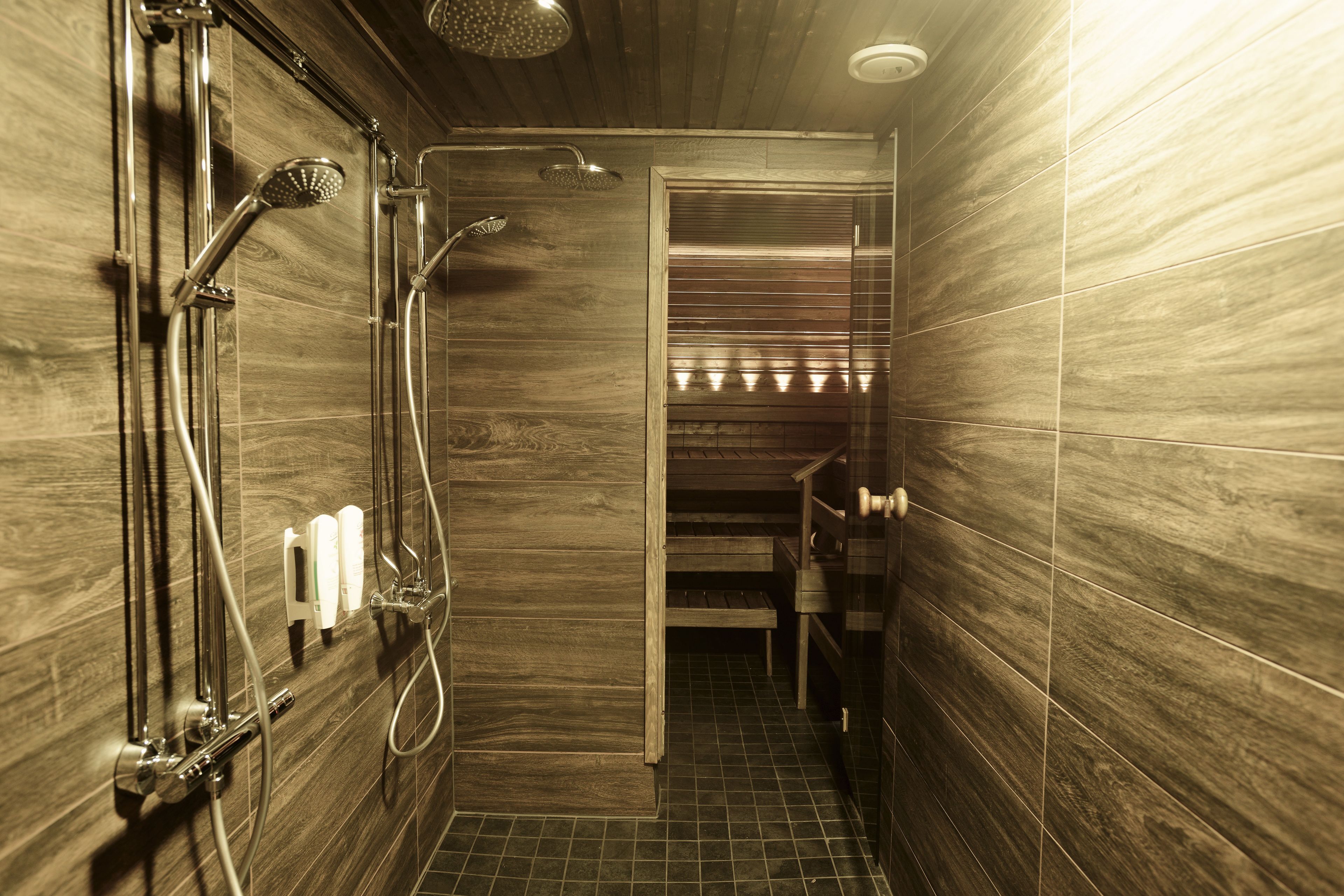 A modern bathroom with a wooden wall, a shower area with chrome fixtures, and a small bench.