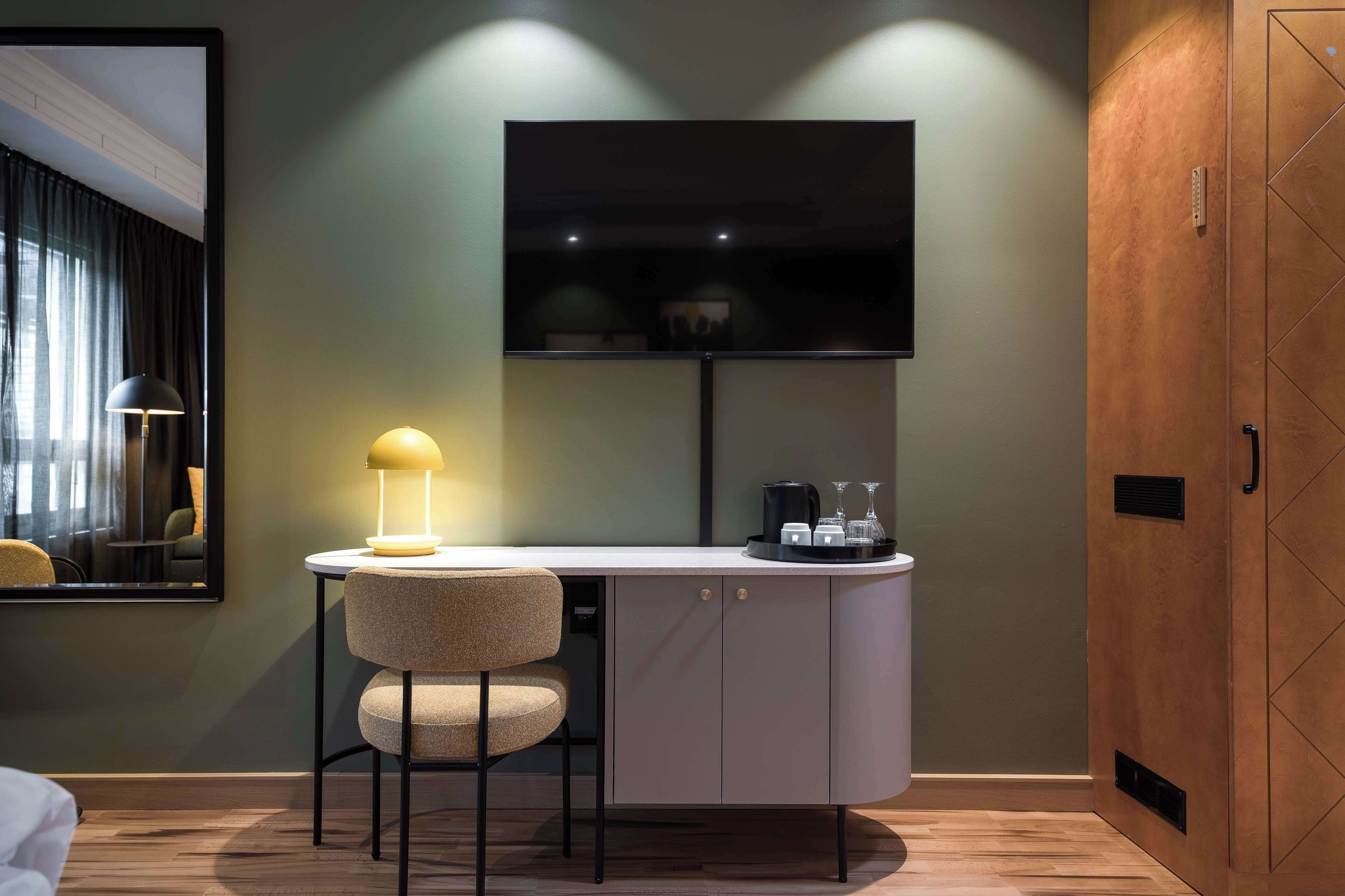 A modern hotel room with a desk, chair, and a flat-screen TV mounted on the wall.