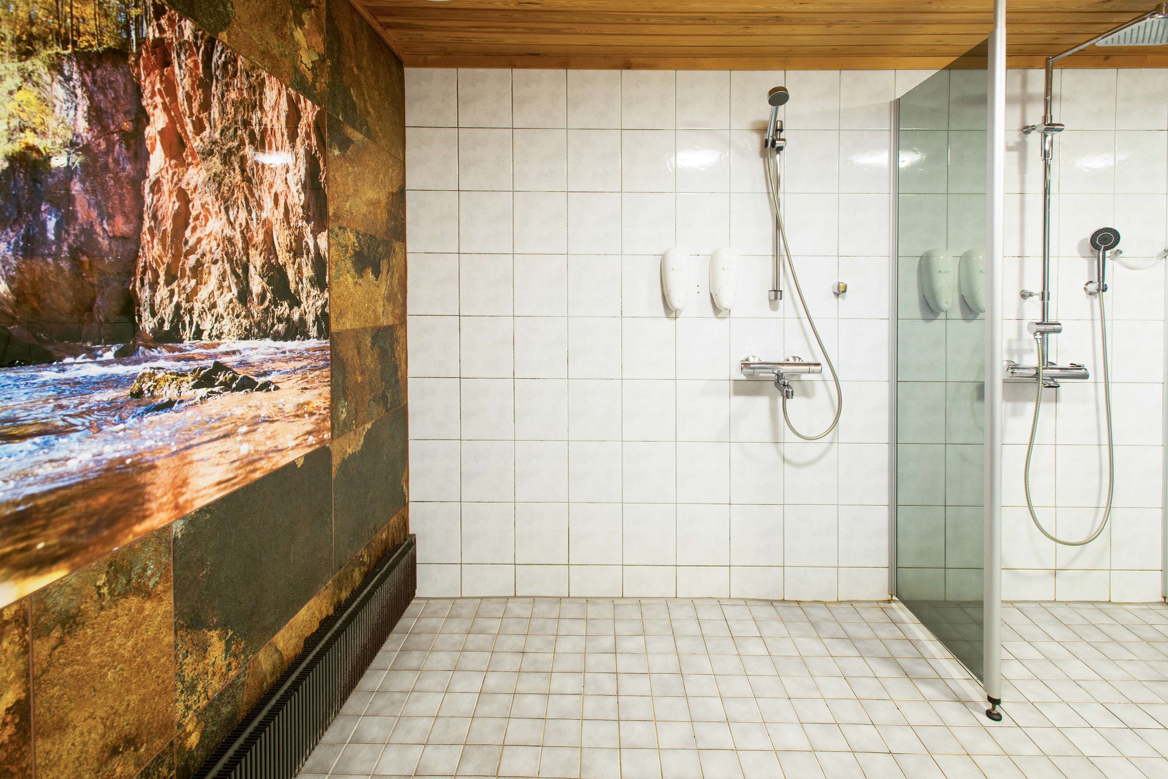 A modern bathroom with a large mural of a rocky landscape, a glass shower enclosure, and white tiled walls.