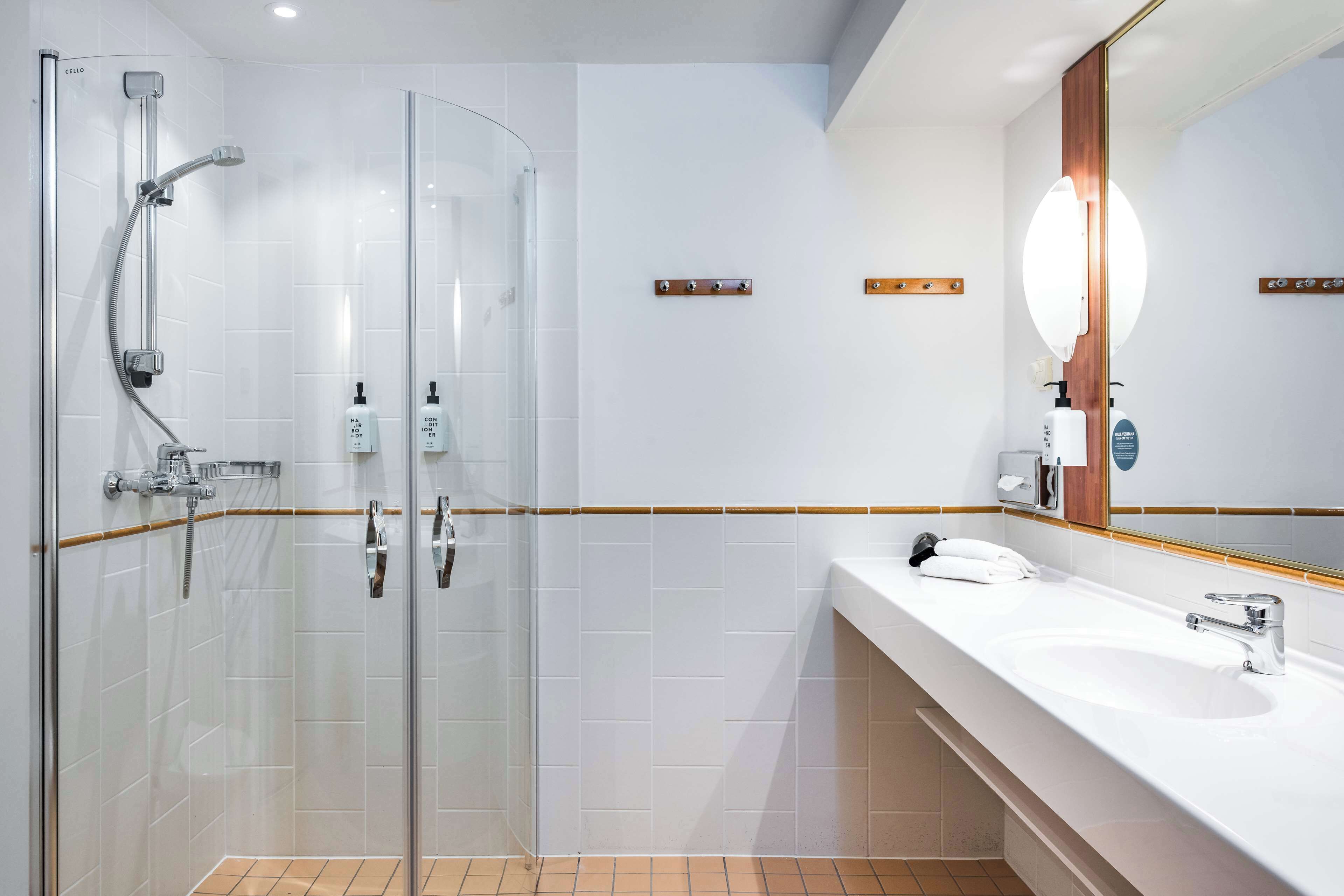 A modern bathroom with a glass-enclosed shower, a white sink, and a large mirror with a wooden frame.