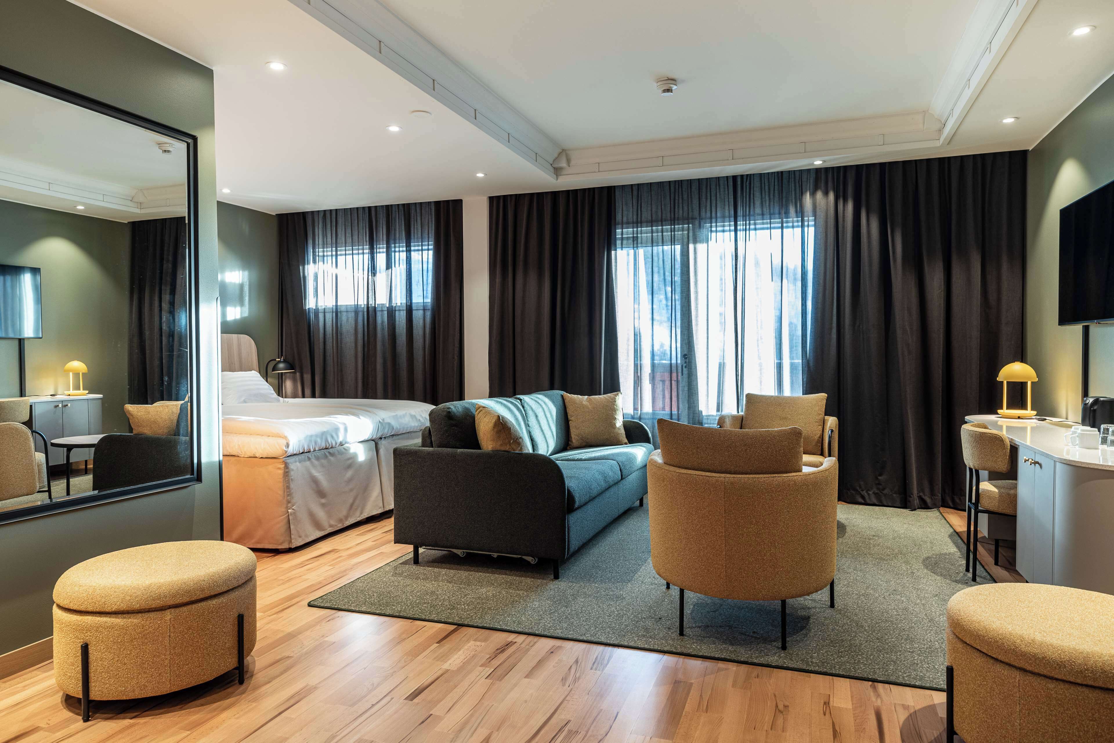 Ein modernes Hotelzimmer mit Bett, Sofa, Sessel und einem kleinen Tisch mit Lampe.