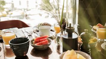 A breakfast table with bowls of fruit, a coffee pot, and a glass of orange juice.