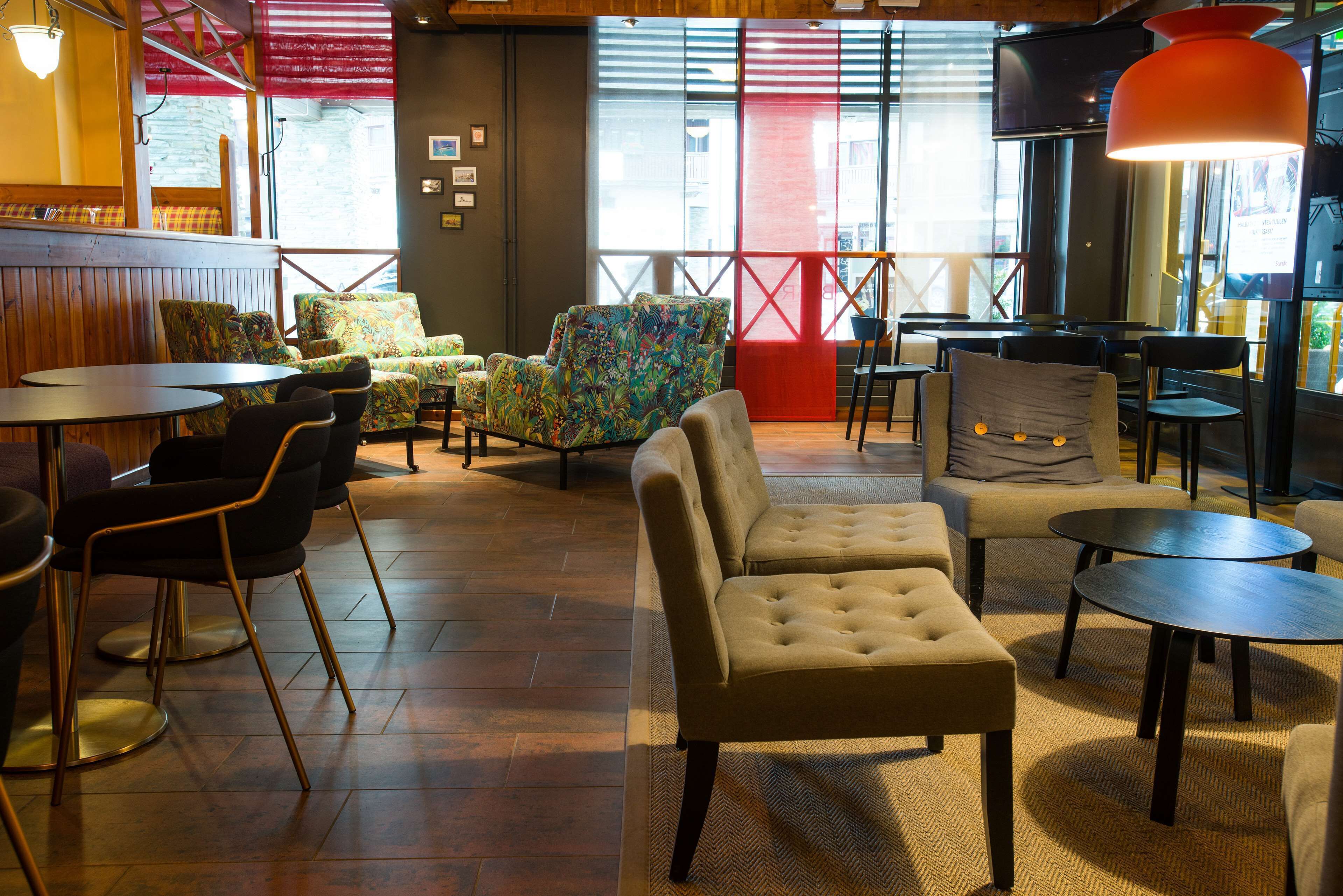 Ein gemütliches Café mit Holztischen und -stühlen, einer großen gepolsterten Couch und einer roten Raumtrennung.