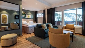 A modern hotel room with a bed, sofa, armchair, and a view of a snowy mountain landscape.