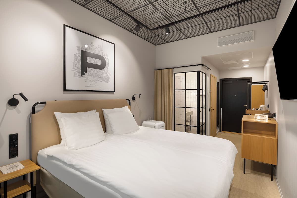 A hotel room with a large bed, a bedside table, a nightstand, a wardrobe, a mirror, and a framed picture on the wall.