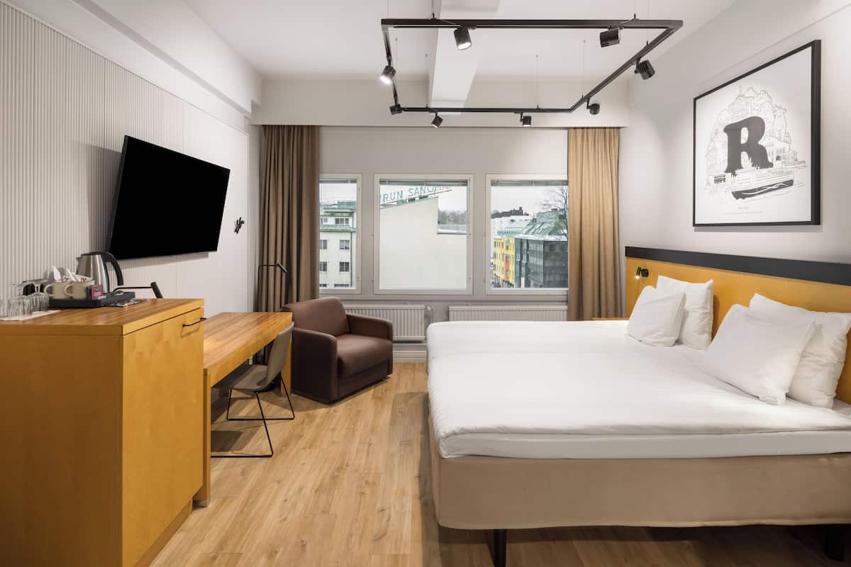 A hotel room with a bed, a desk, a chair, a flat-screen TV, and a window with a city view.