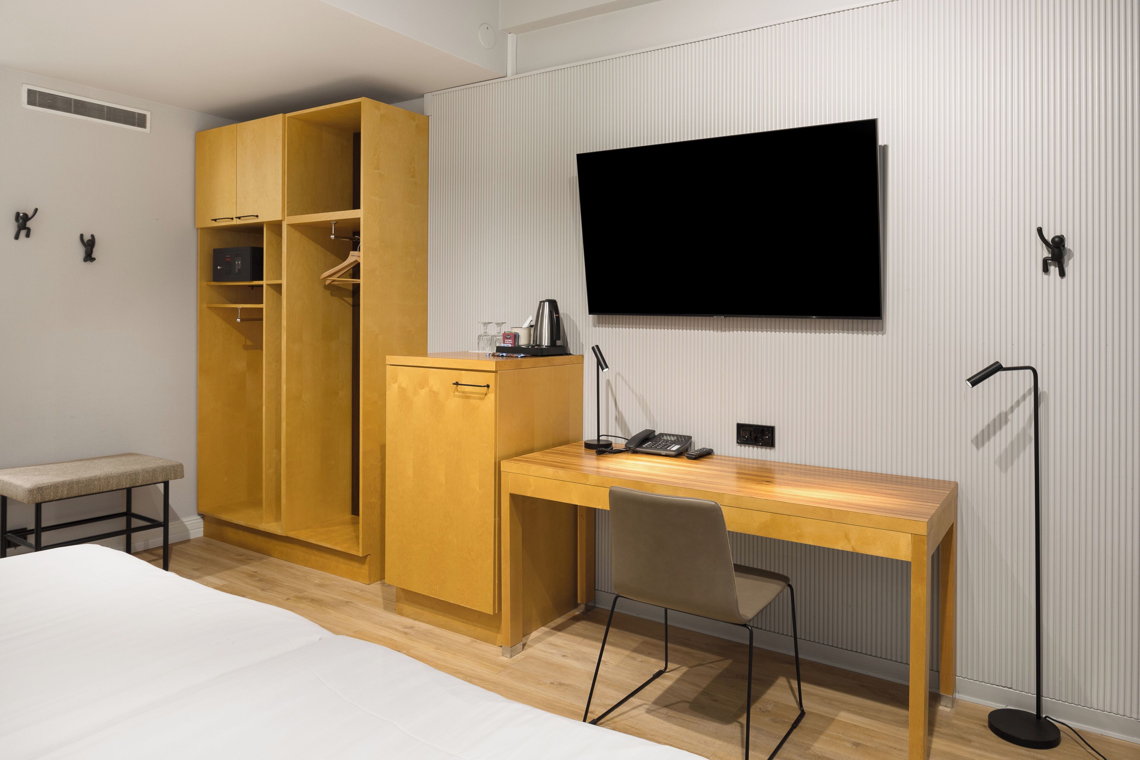 Habitación de hotel con un escritorio de madera, una silla, una cama, un armario, un televisor de pantalla plana y una lámpara de pie.
