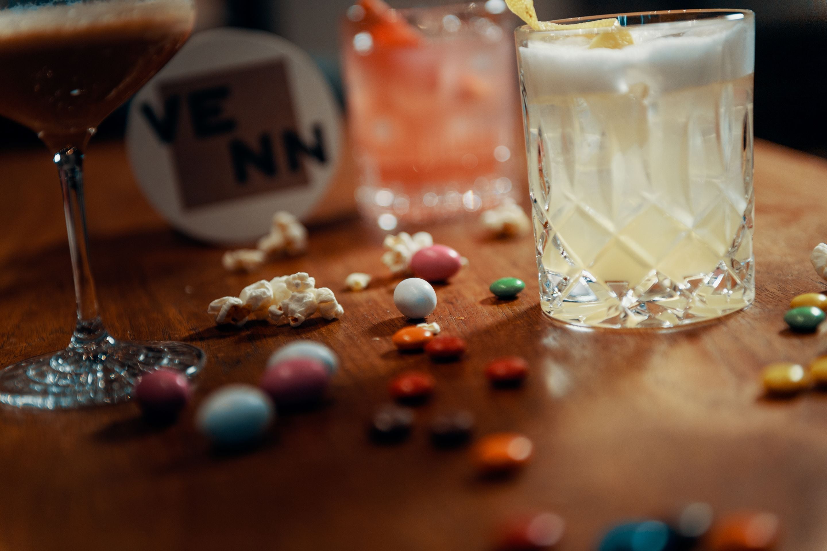 A wooden table with two glasses of beverages, colorful candies, and a small decorative item.