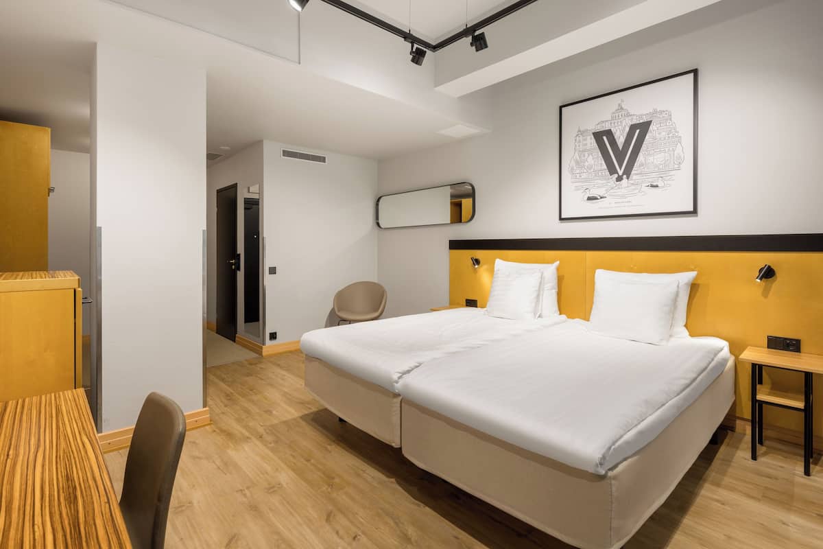 A modern hotel room with a large bed, a desk, a chair, and a mirror on the wall.