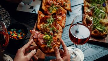 Ruokapöydällä on pizzaa, lasillinen viiniä ja kulho värikkäitä makeisia.