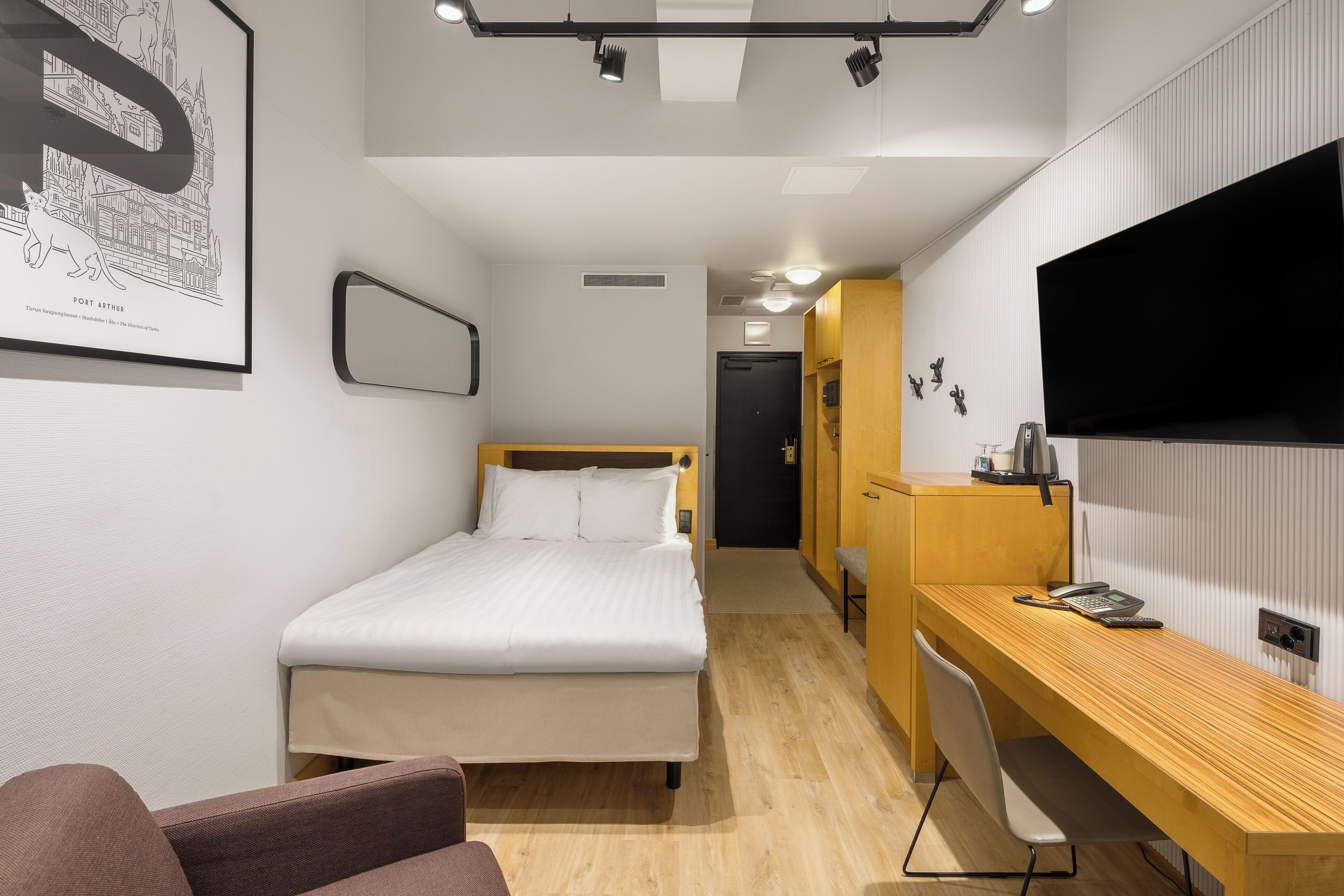 A modern hotel room with a bed, a desk, a chair, a TV, and a framed picture on the wall.
