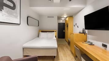 A modern hotel room with a bed, a desk, a chair, a TV, and a framed picture on the wall.