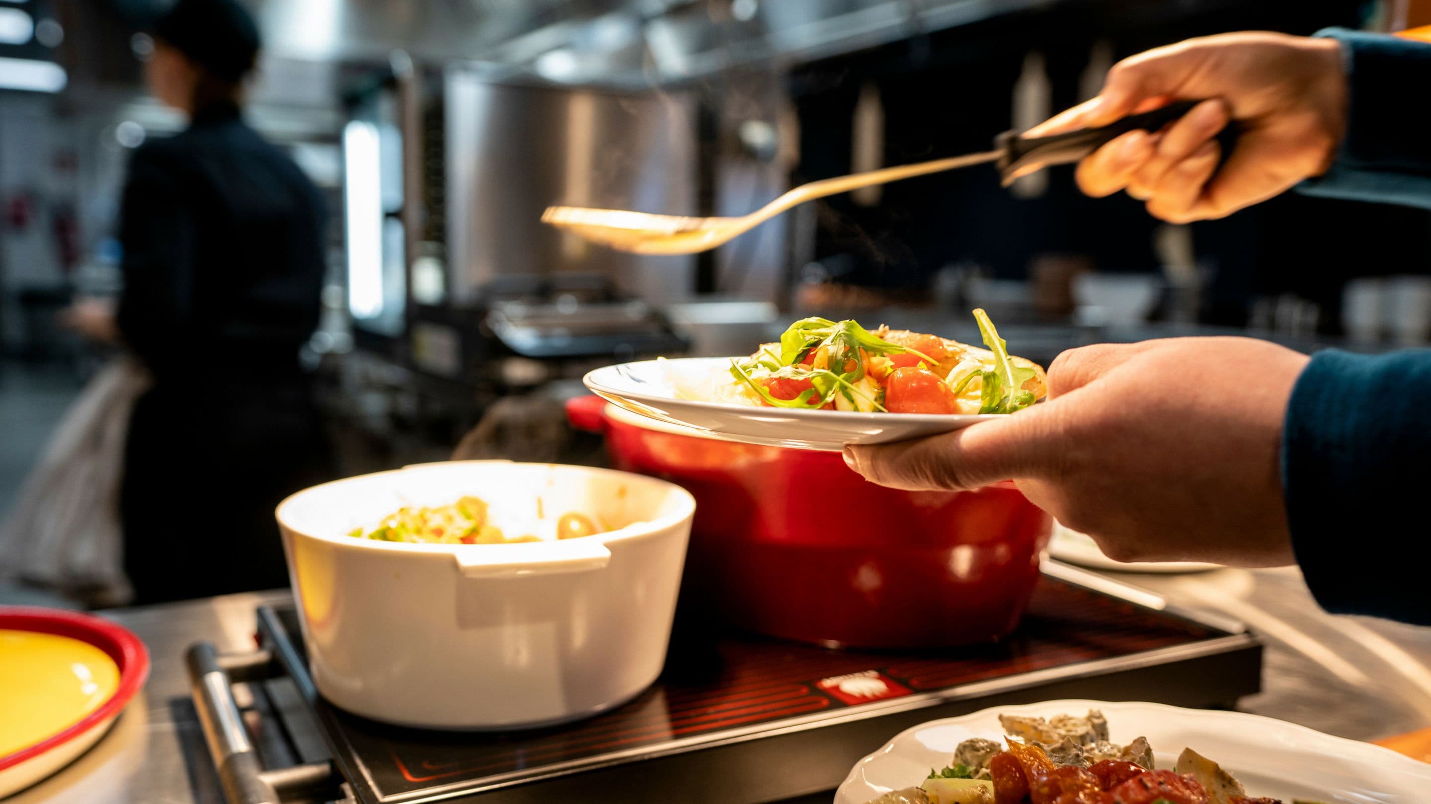 A person serving food from a red pot to a white bowl on a tray.
