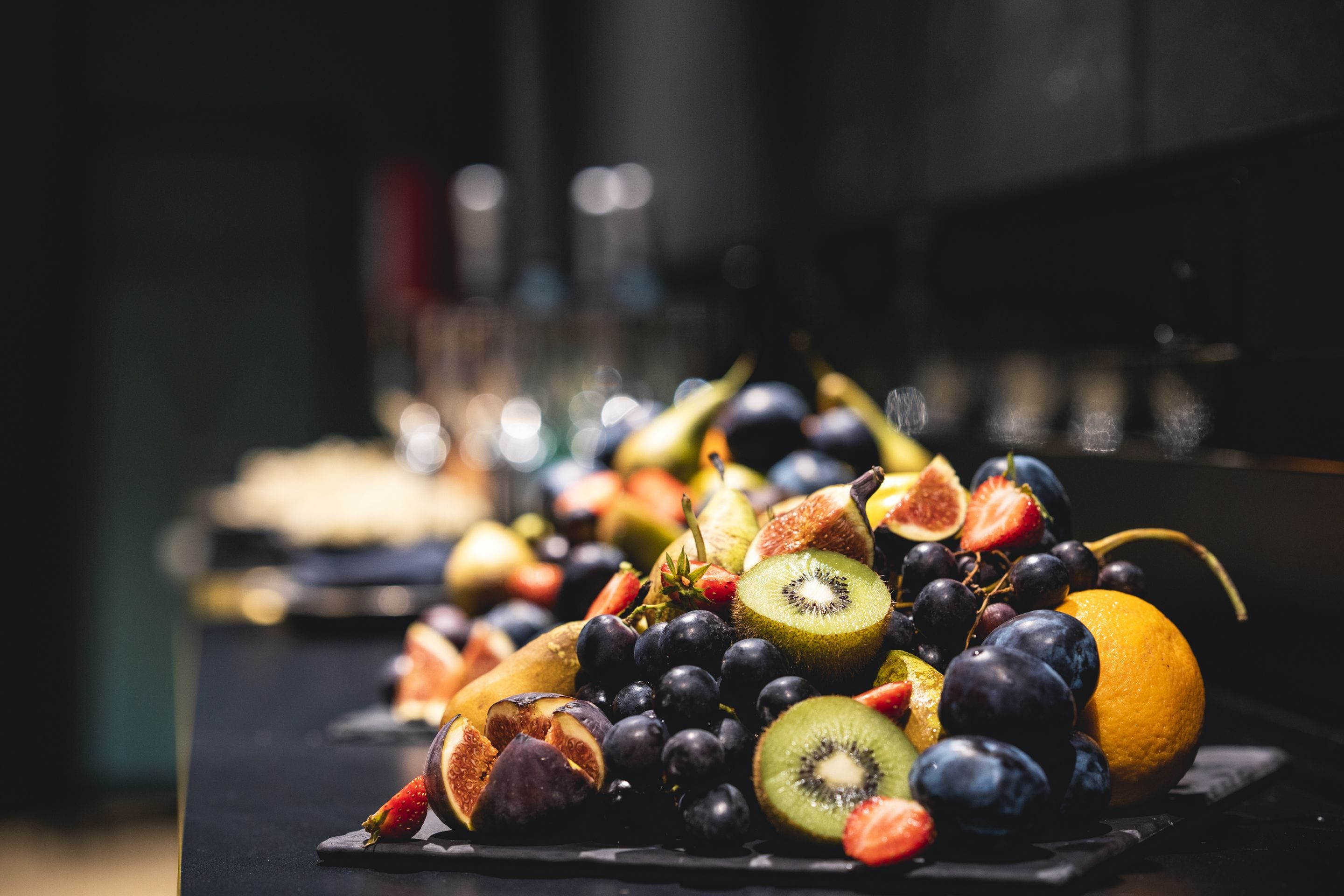 A variety of fruits including grapes, kiwis, figs, and oranges arranged on a dark surface.