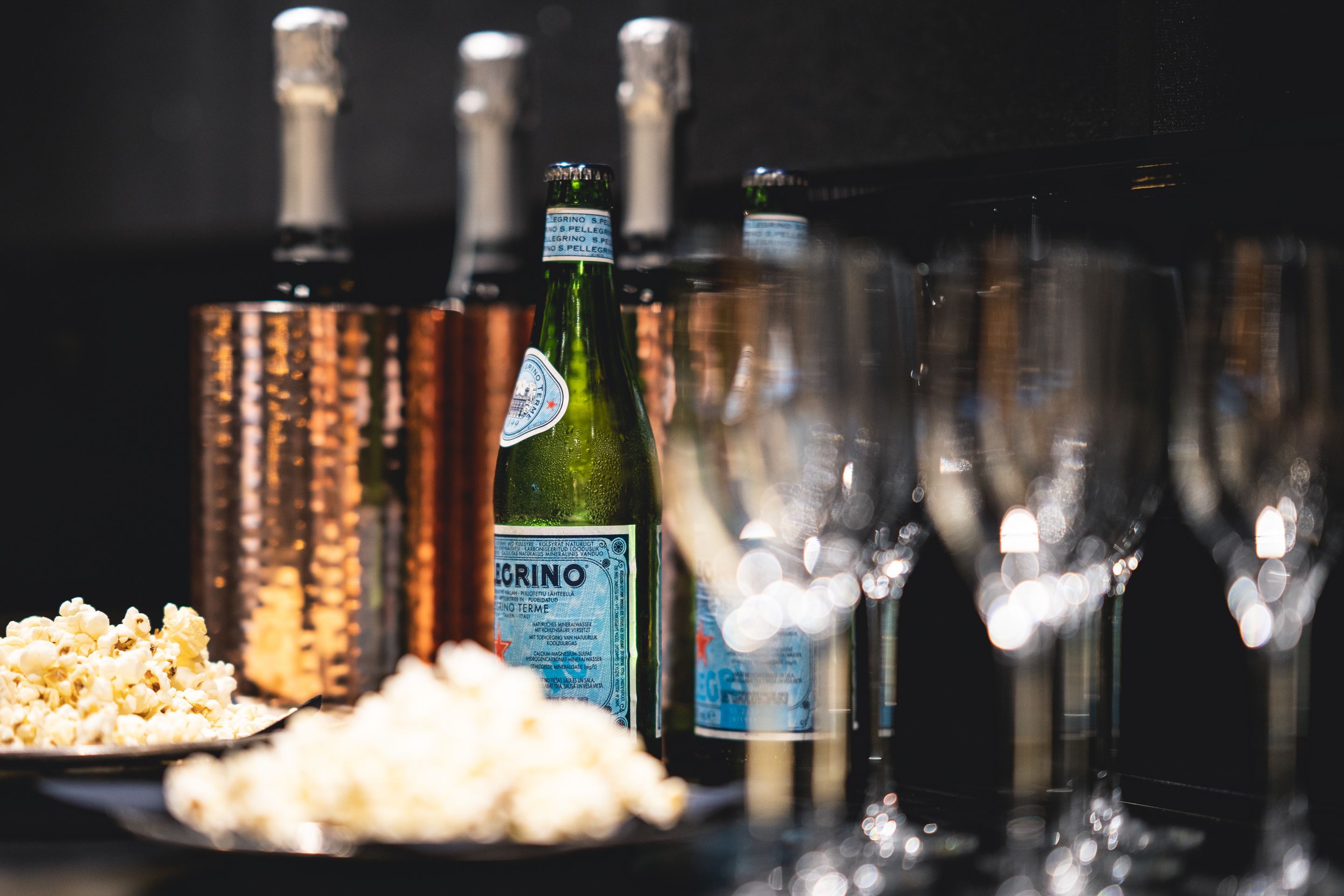 A table with bottles of wine, glasses, and a plate of popcorn.