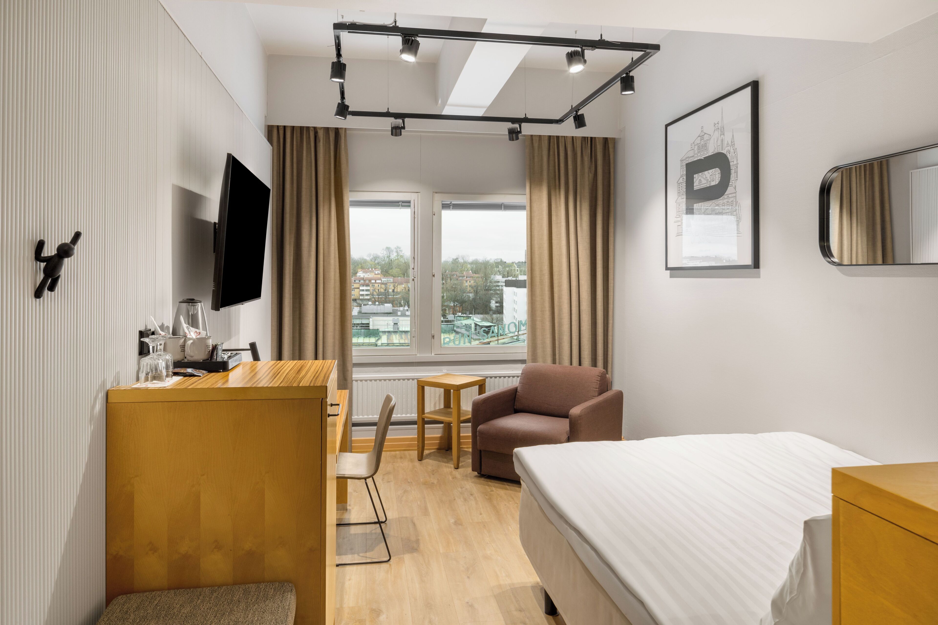 Una habitación de hotel moderna con una cama, un escritorio, una silla, un sofá, un televisor y una ventana con vistas a la ciudad.