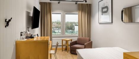 Una habitación de hotel moderna con una cama, un escritorio, una silla, un sofá, un televisor y una ventana con vistas a la ciudad.