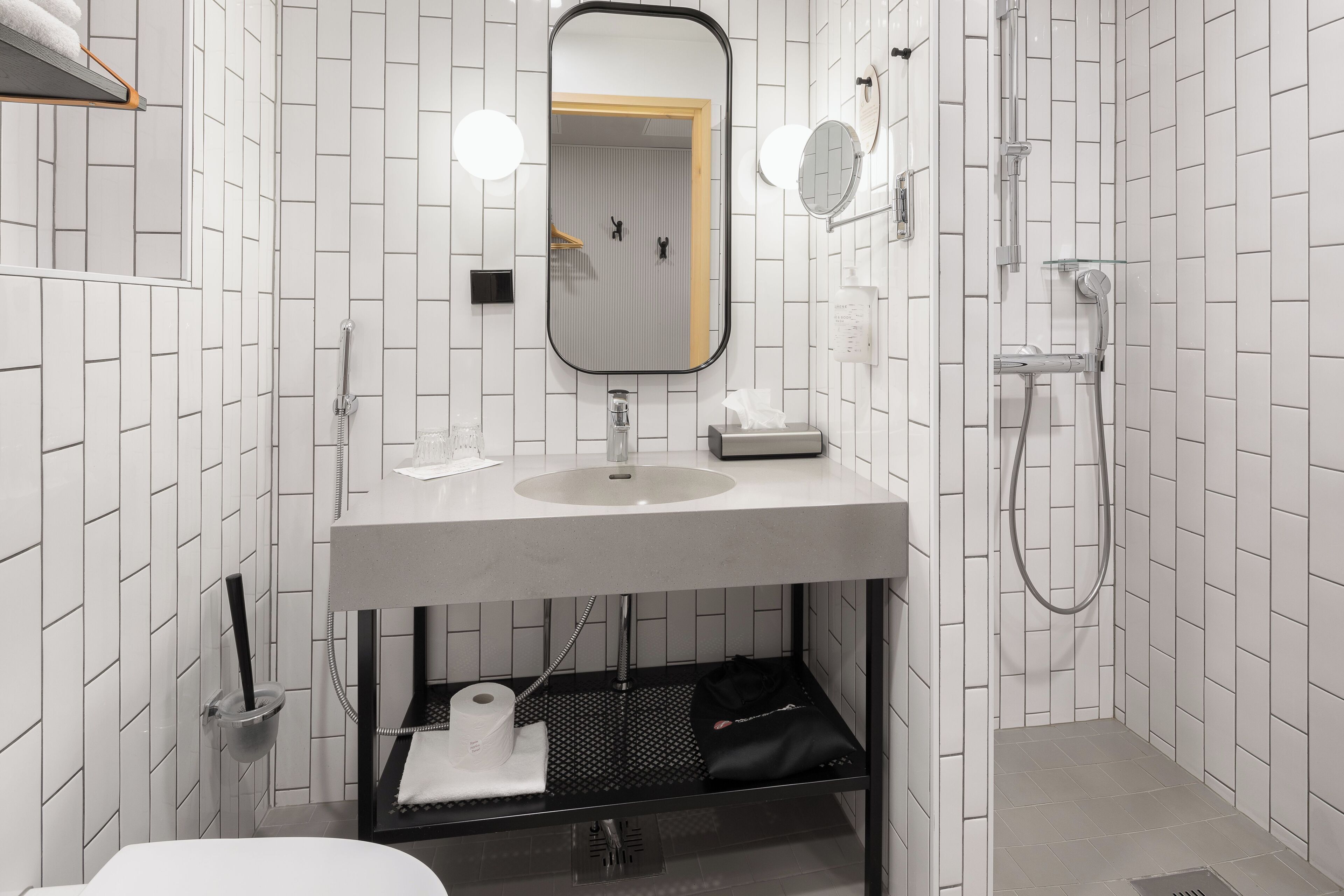 A modern bathroom with a white tiled wall, a sink with a mirror, a shower, and a towel rack.