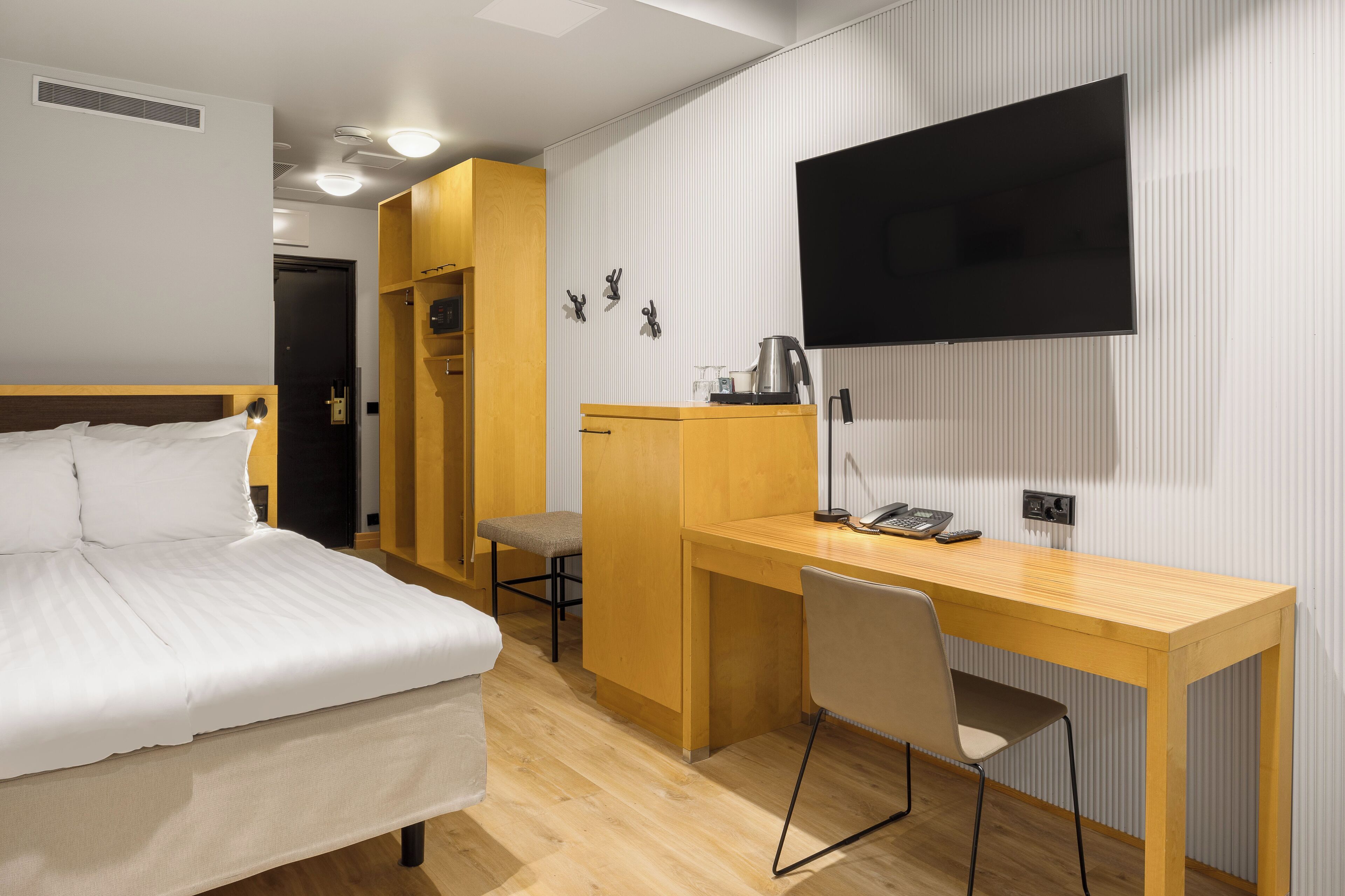 Habitación de hotel con cama, escritorio, silla, televisor y kitchenette.