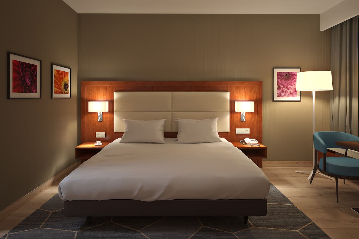 Een hotelkamer met een groot bed, twee nachtkastjes met lampen, een stoel en kunstwerken aan de muren.