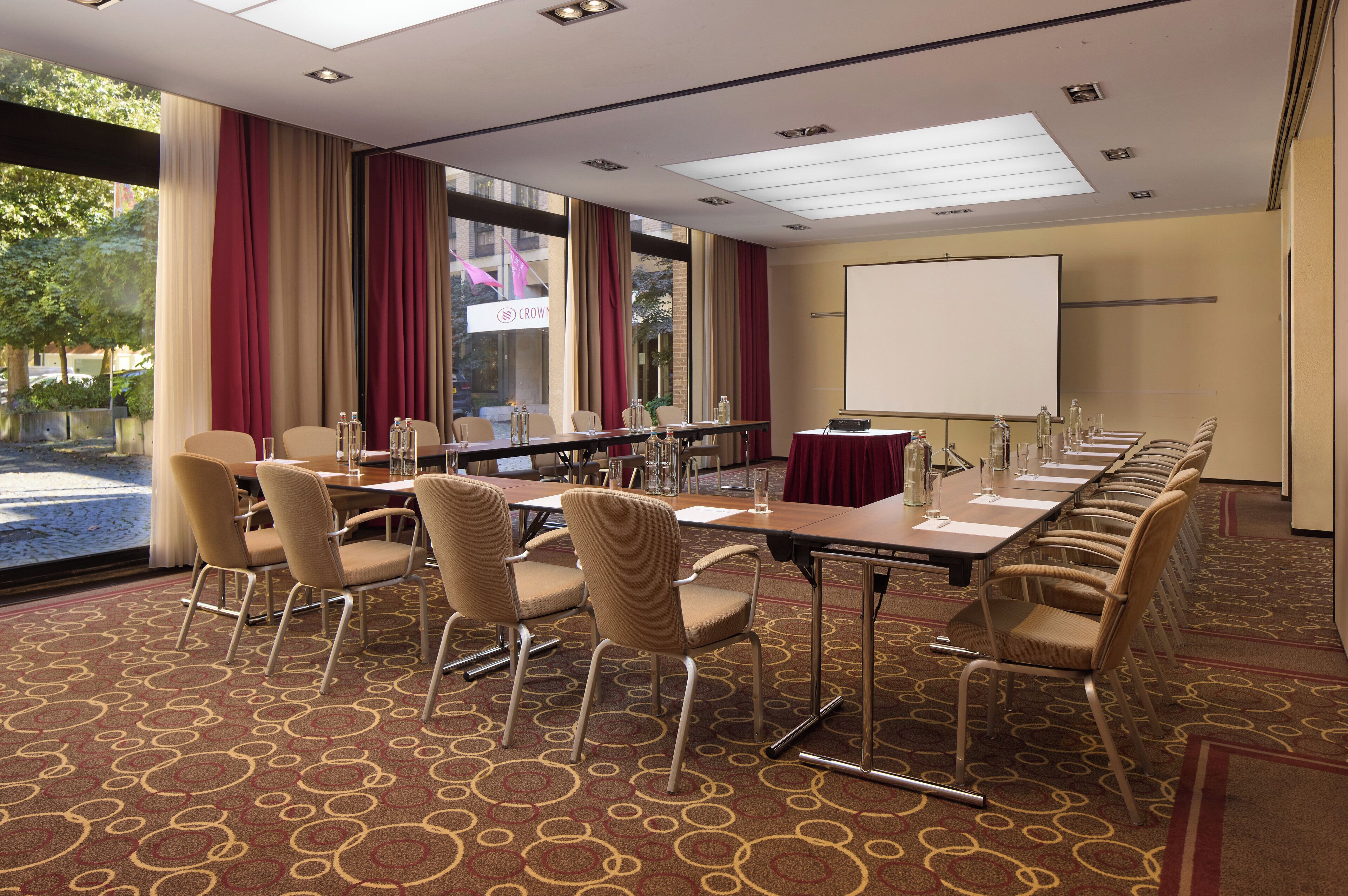 A conference room with a long table, chairs, a projector screen, and a view of the outdoors.