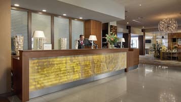 A hotel reception area with a modern design, featuring a reception desk, two lamps, and a decorative wall.