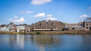 Un hôtel situé au bord de l’eau, composé de plusieurs bâtiments, avec une rivière au premier plan et un ciel dégagé.