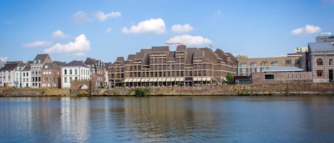 A waterfront hotel with multiple buildings, a river in the foreground, and a clear sky.