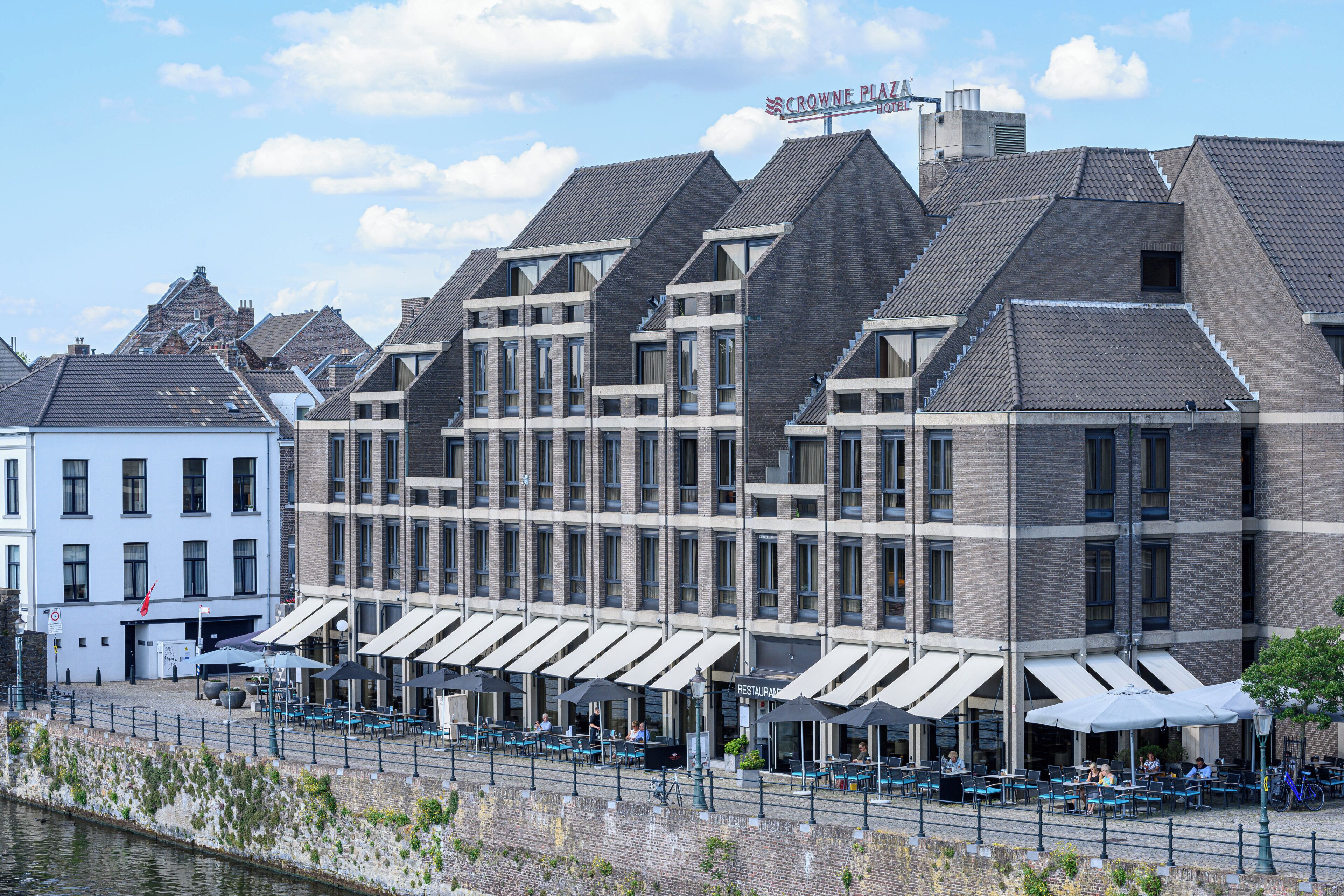 A hotel with a modern architectural design, featuring a prominent sign, outdoor seating area with umbrellas, and a waterfront view.