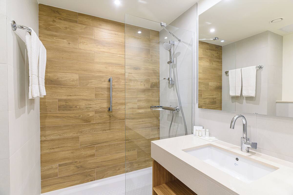 A modern bathroom with a wooden wall, a glass-enclosed shower, a white sink, and a large mirror.