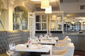 Un restaurant doté de banquettes grises à motifs capitonnés, de tables blanches ornées de verres, et d’un décor intérieur moderne.