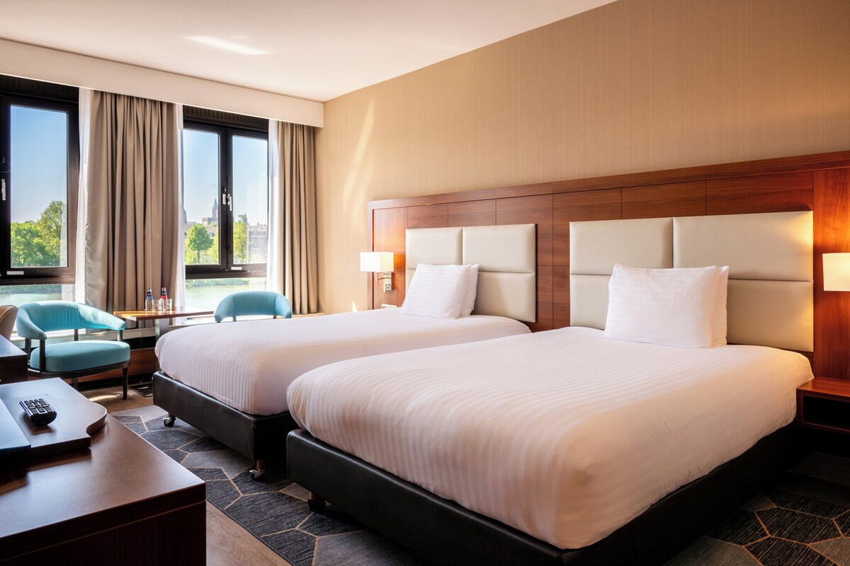 Ein Hotelzimmer mit zwei Betten, einem Schreibtisch, einem Stuhl und Blick ins Freie.