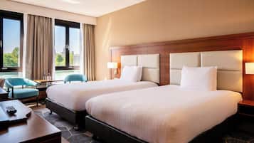 A hotel room with two beds, a desk, a chair, and a view of the outdoors.