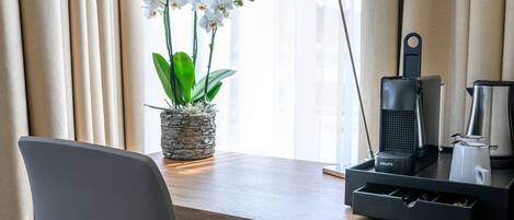 Habitación de hotel con un escritorio de madera, una orquídea en maceta, una cafetera Krups y una lámpara.