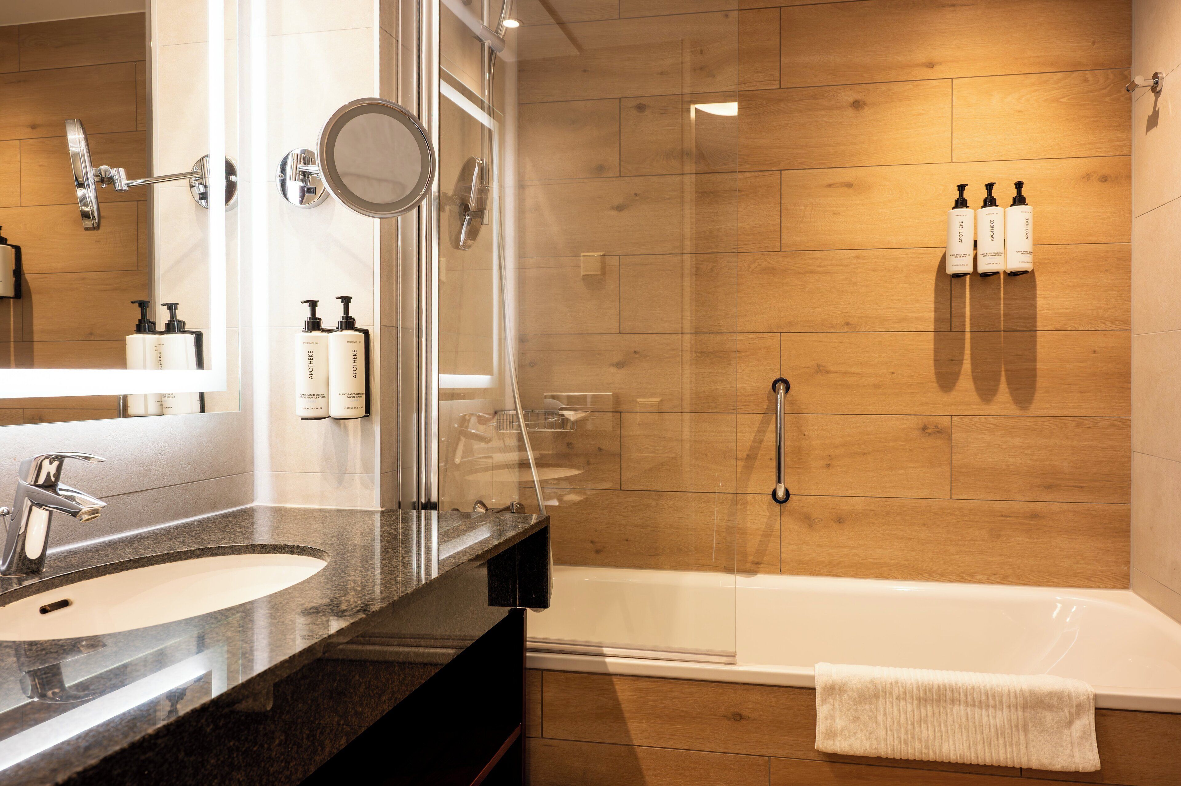 A modern bathroom with two sinks, a large mirror, a shower with a glass door, and wooden paneling on the walls.